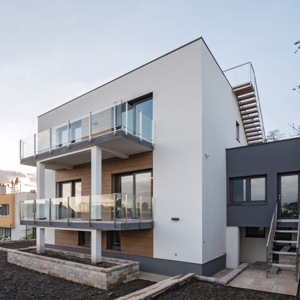 A modern two-story white and dark gray building with glass-railed balconies and an external wooden staircase.