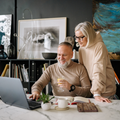 Two people collaborating at a desk with a laptop, papers, and coffee in a modern office