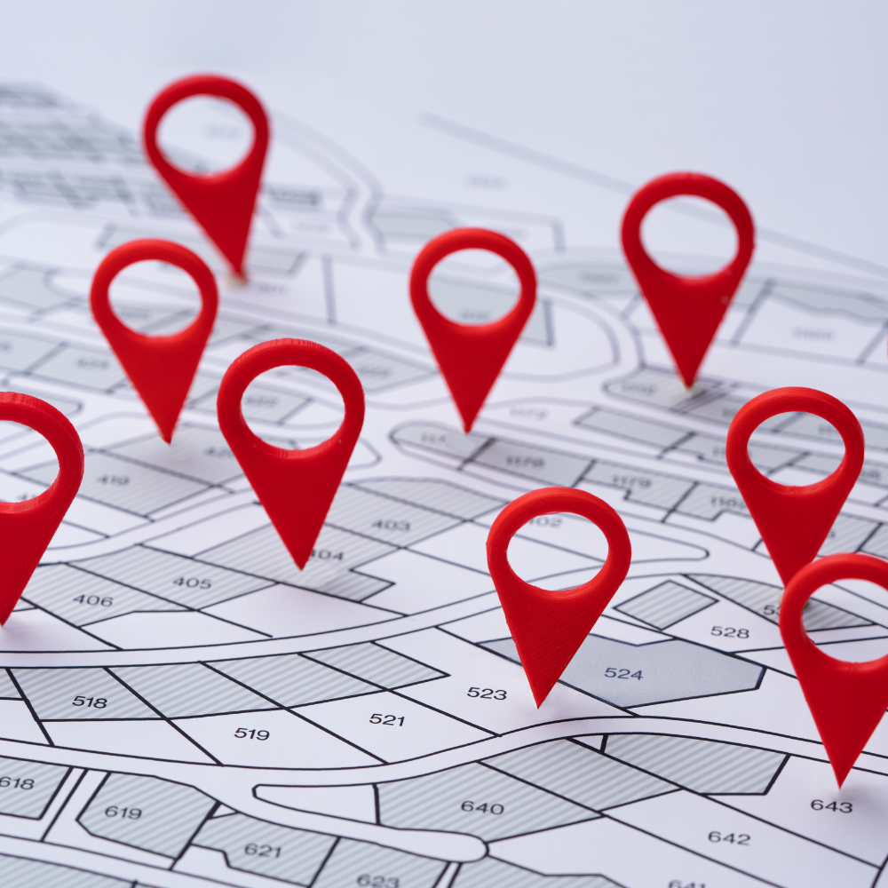 Several red map pins are placed on different plots of a printed land survey map.