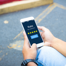 A person holds a smartphone displaying a five-star rating screen with a submit button, set against a blurry urban background.