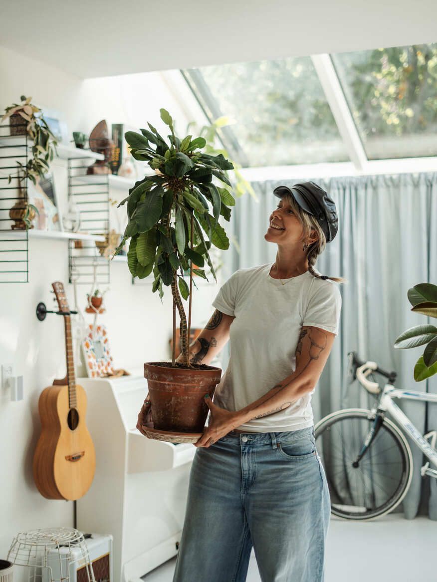 A woman is holding a potted plant in a living room.