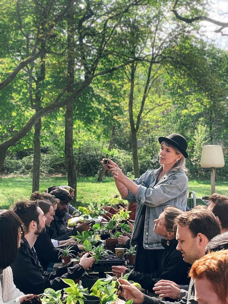 A woman is standing in front of a group of people holding plants.
