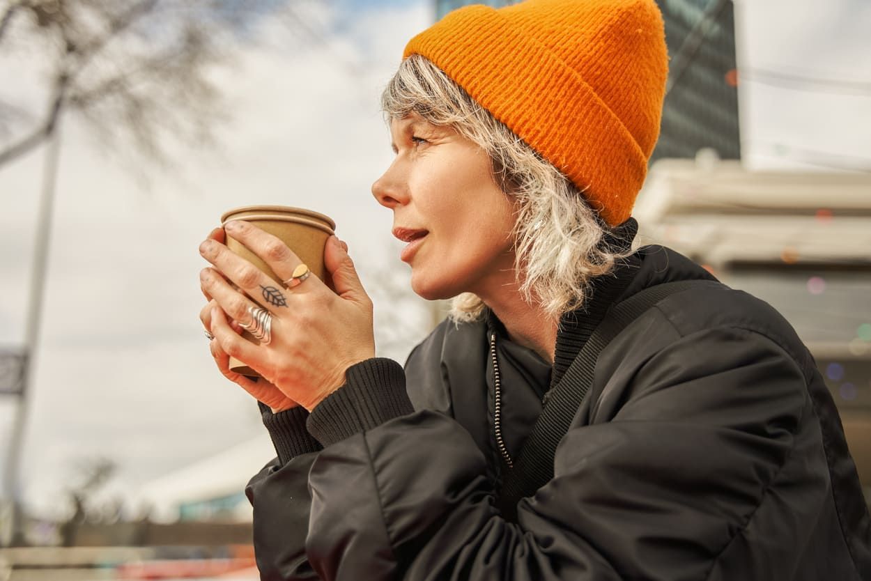a woman wearing an orange beanie is holding a cup of tea .