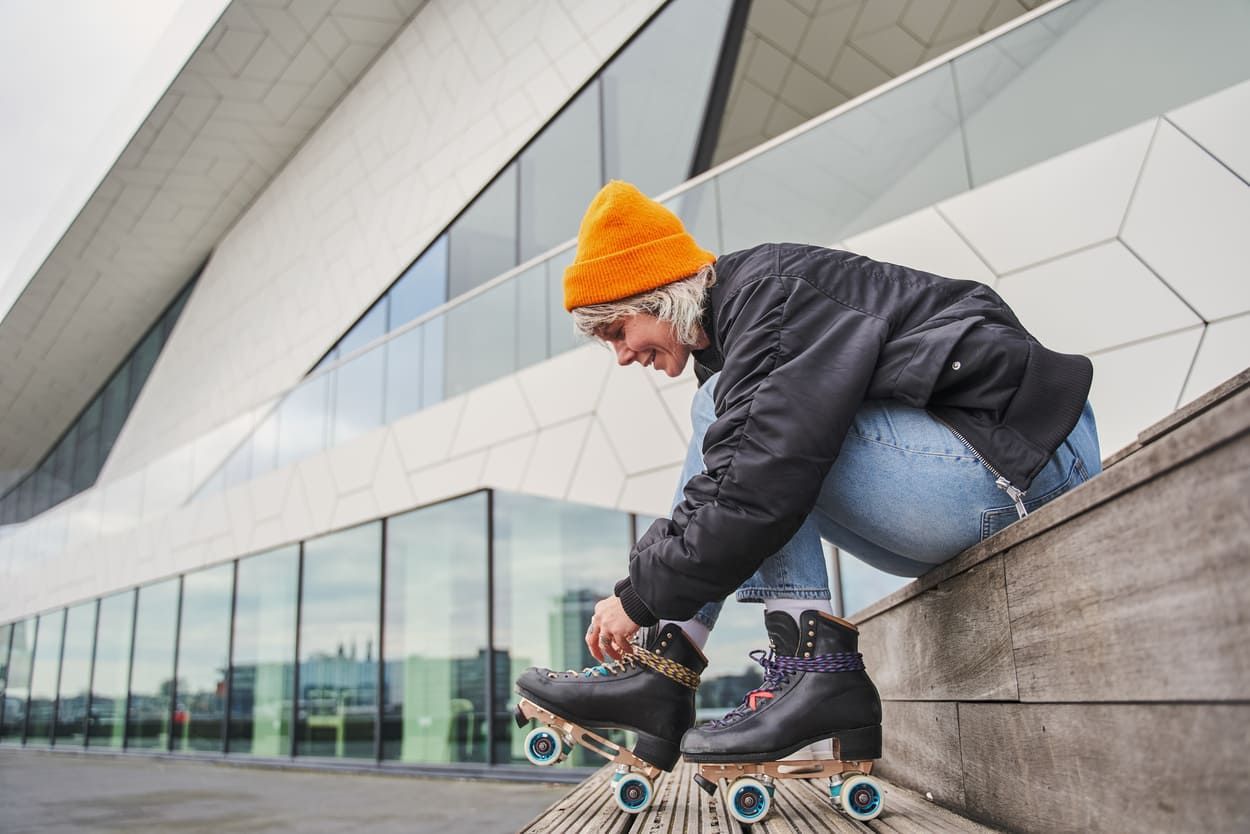 a woman is sitting on a wooden ledge tying her roller skates .