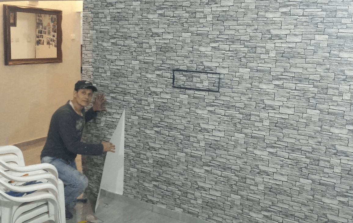 A man is sitting on a chair in front of a brick wall.