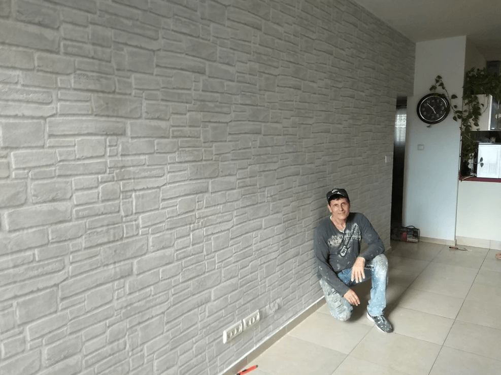 A man is kneeling in front of a brick wall in a living room.