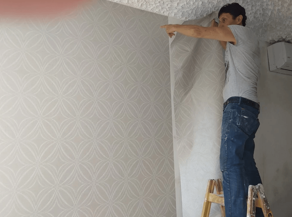 A man is standing on a ladder peeling off a piece of wallpaper