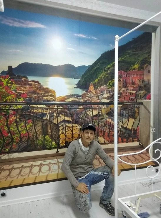 A man is kneeling in front of a painting of a landscape