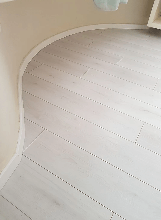 A white wooden floor with a curved corner in a room.