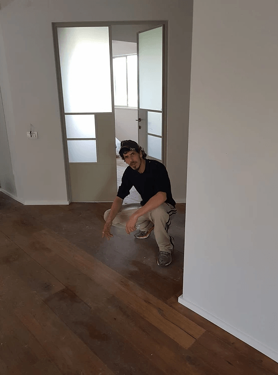 A man is kneeling on a wooden floor in an empty room.