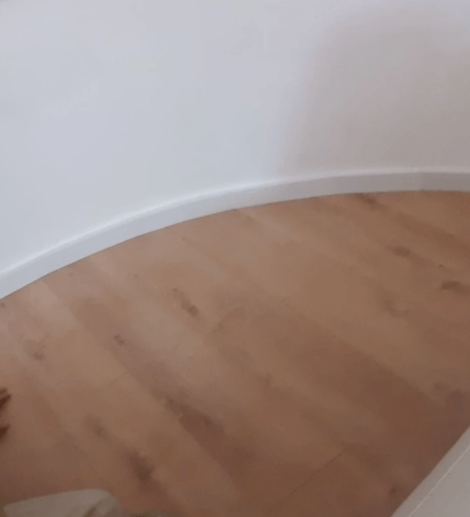 A close up of a wooden floor in a room with a white wall.