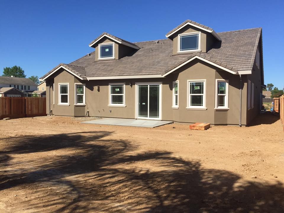 Back of a brown stucco house with a new concrete patio and windows on a sunny day.