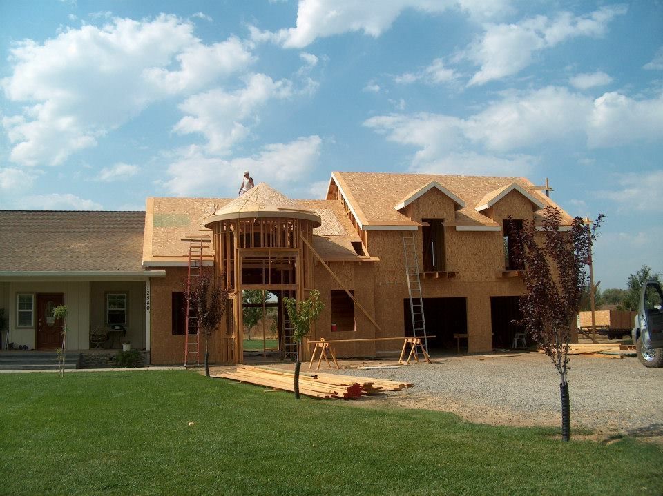 House under construction, wood framing with roof and tower, blue sky, green grass.