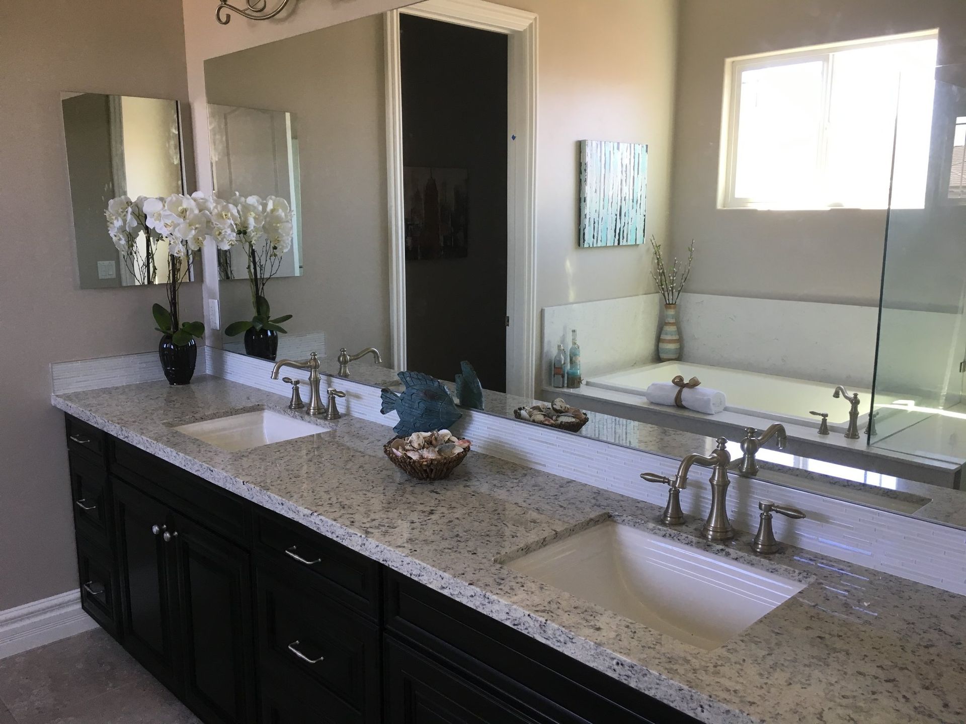 Bathroom with double vanity, black cabinets, granite countertop, and large mirrors.