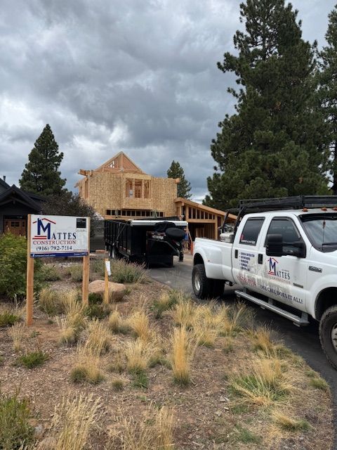 Construction site with partially framed house, trailer, white truck, and sign. Cloudy day.