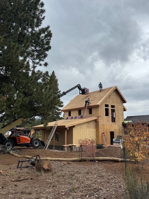 Construction of a two-story house with workers on the roof, using a lift. Overcast day.