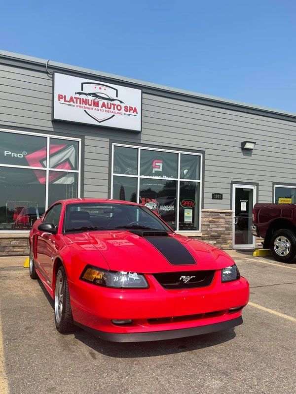 Red Mustang car parked in front of Platinum Auto Spa building with a black stripe on the hood.