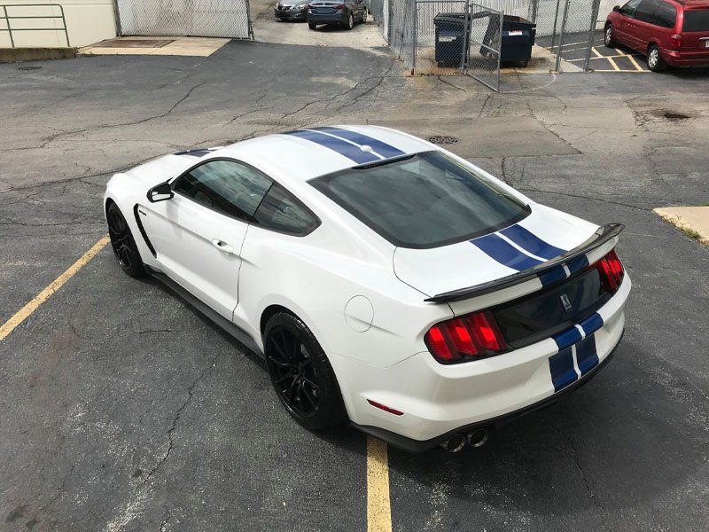 White Ford Mustang with blue racing stripes, parked in a lot.