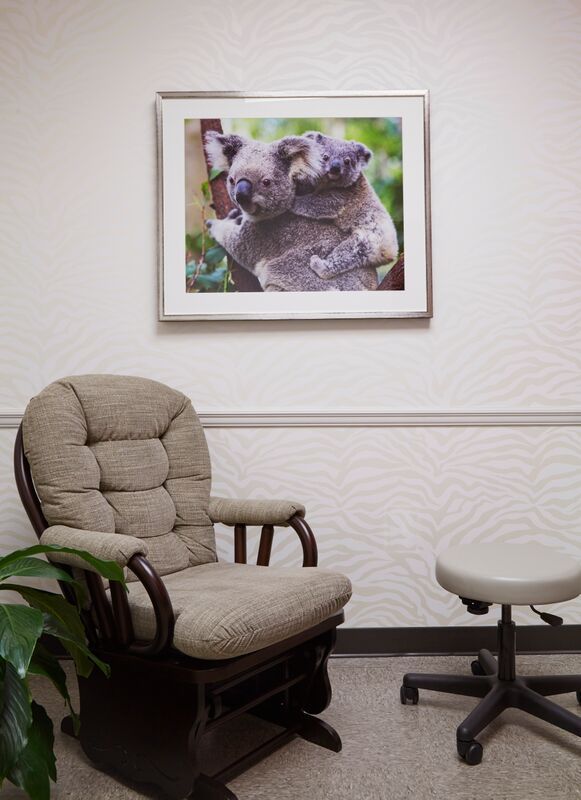 A room with a rocking chair and a picture of two koalas on the wall
