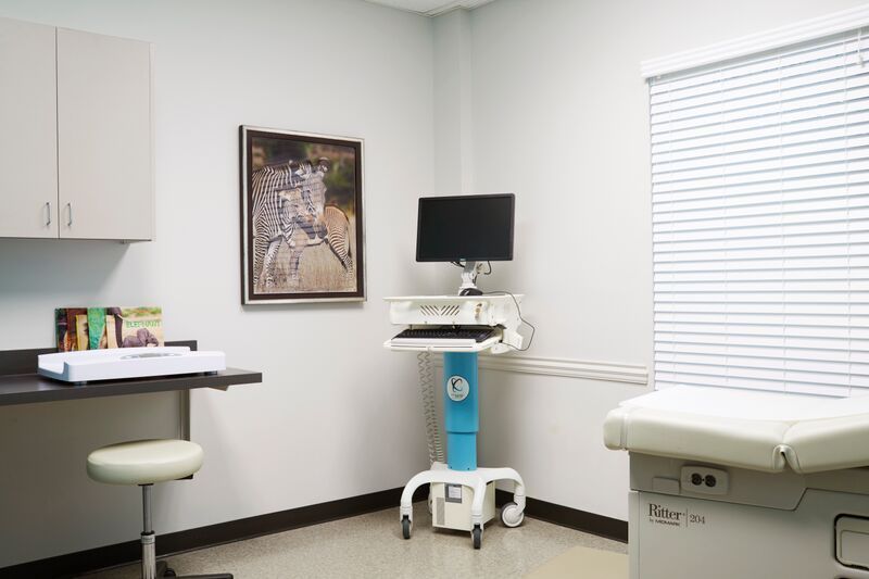 A doctor 's office with a desk , stool , computer and a picture on the wall.