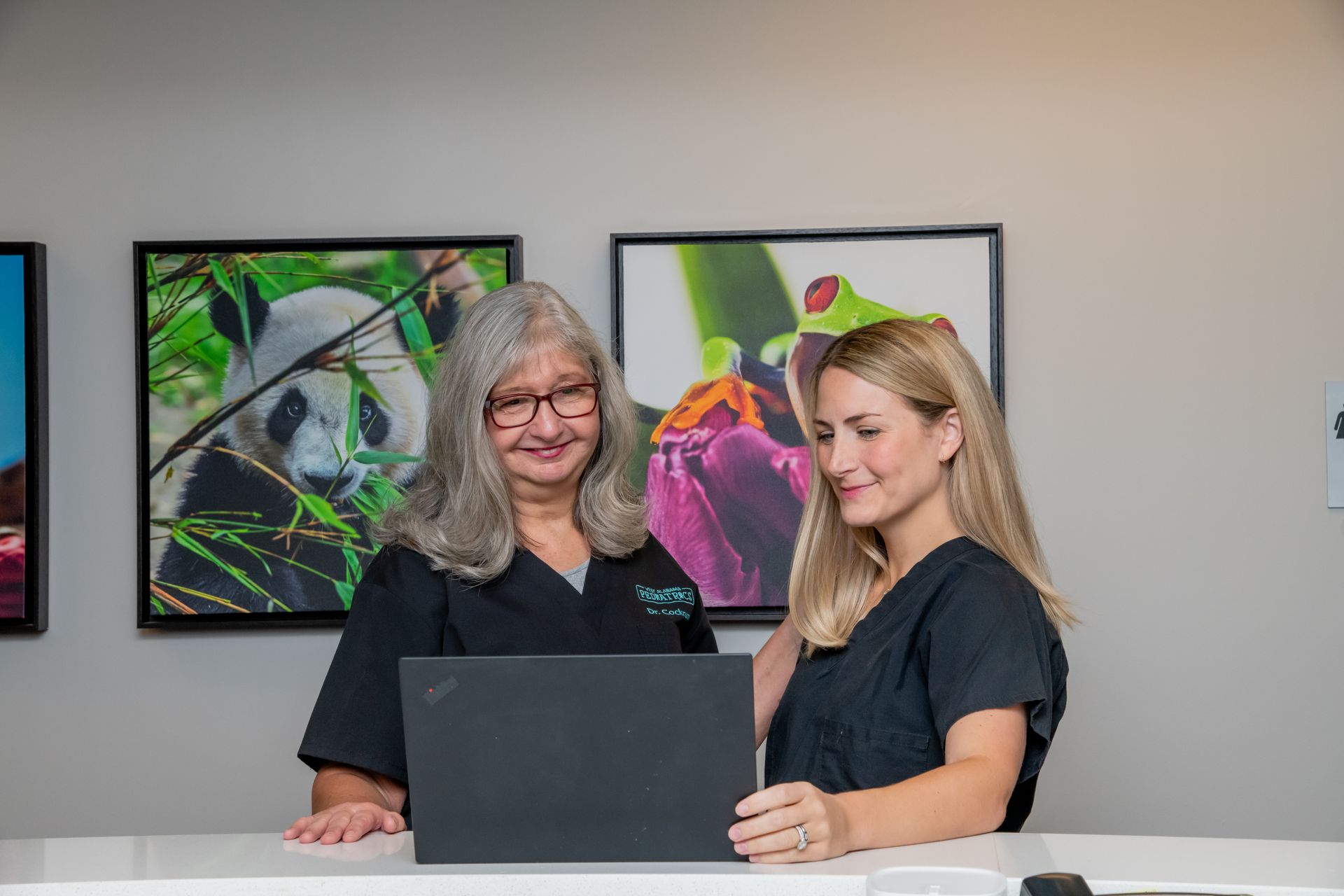 Two women are standing next to each other looking at a laptop computer.