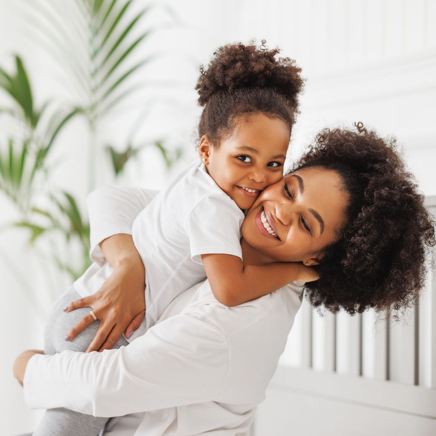 Woman hugging smiling child on a white couch in a bright room