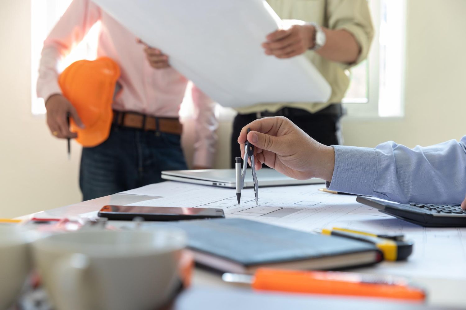 Arquitectos revisando planos, usando una brújula, con herramientas y una computadora portátil sobre una mesa.