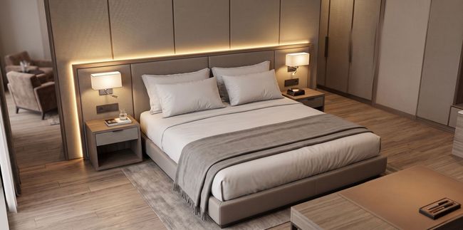Moderne slaapkamer met een groot gestoffeerd bed, sfeervolle nachtlampjes en een neutrale beige inrichting.