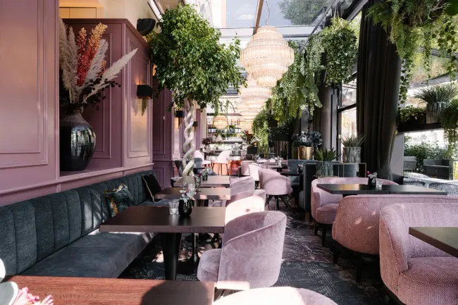 Stijlvol terras met roze en groene decoratie onder hangende planten en kroonluchters.
