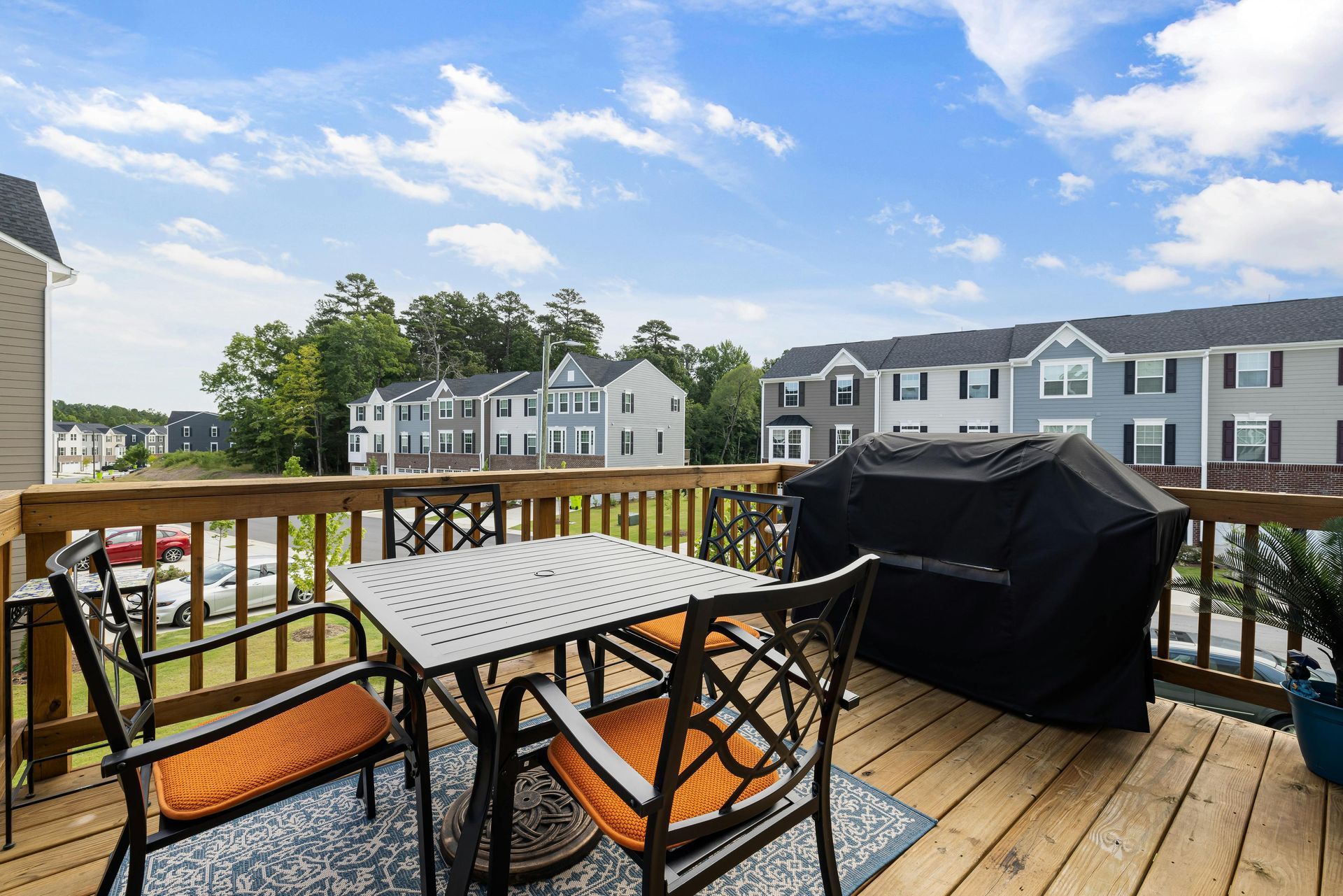 Deck with patio table, chairs, grill, and waterfront townhouses under a partly cloudy sky