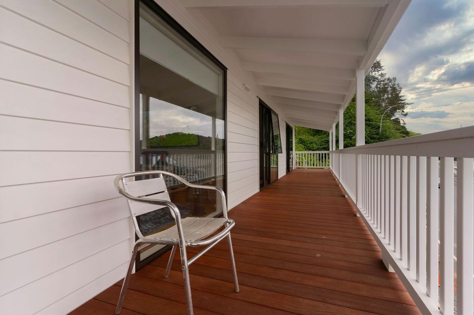 White porch with red wooden floor, white railing, and a metal chair beside a house.