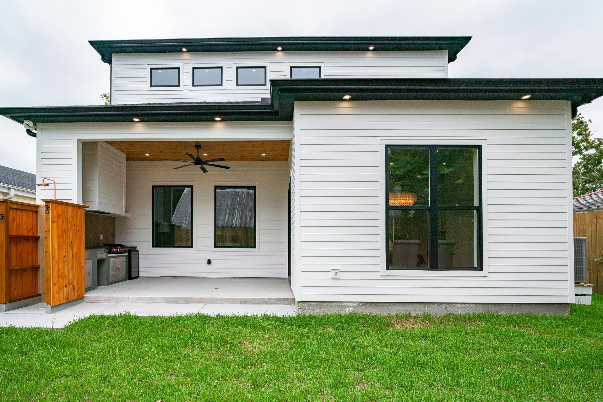 Modern white house exterior with covered patio, large windows, and green lawn