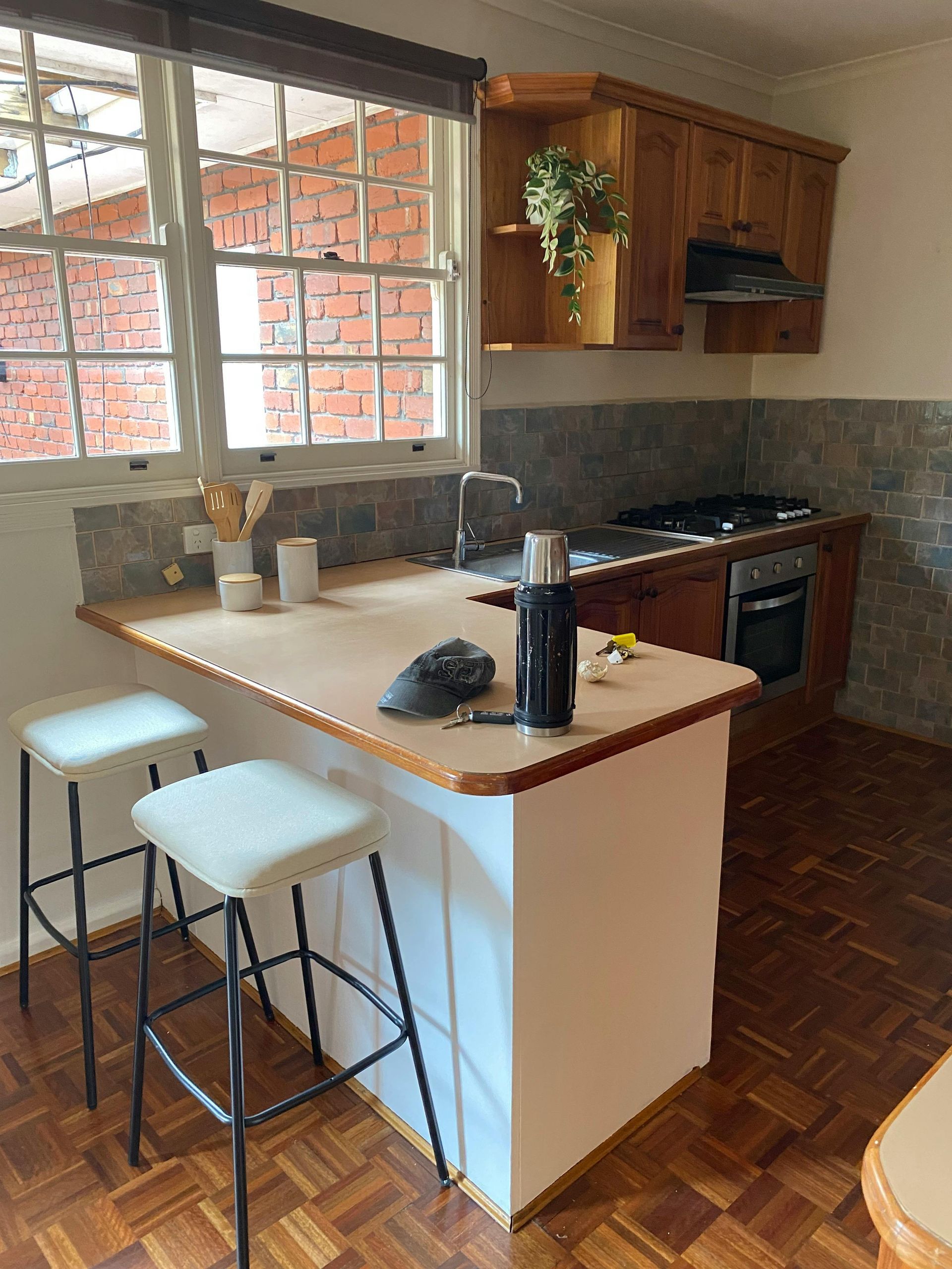 Small kitchen with white island, two stools, wooden cabinets, and a window over the sink.