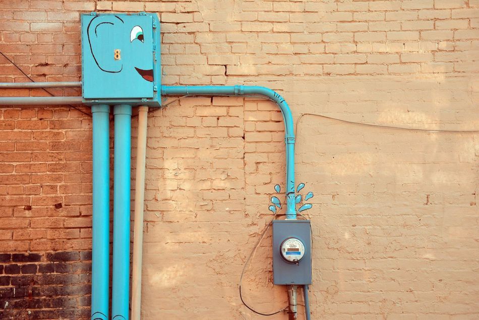 Turquoise electrical boxes and conduit mounted on a brick wall
