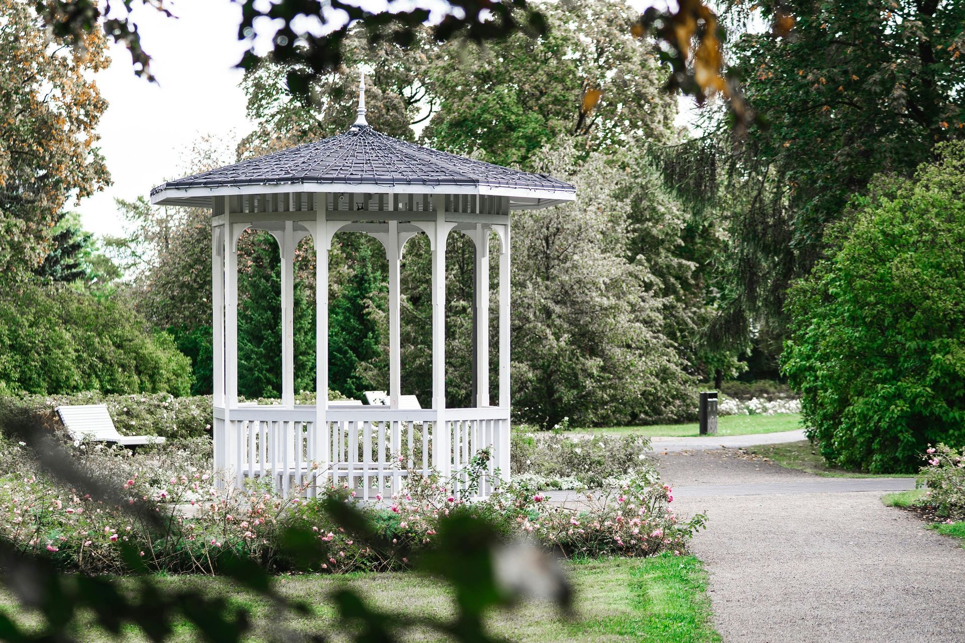 White gazebo in a lush garden beside a winding gravel path