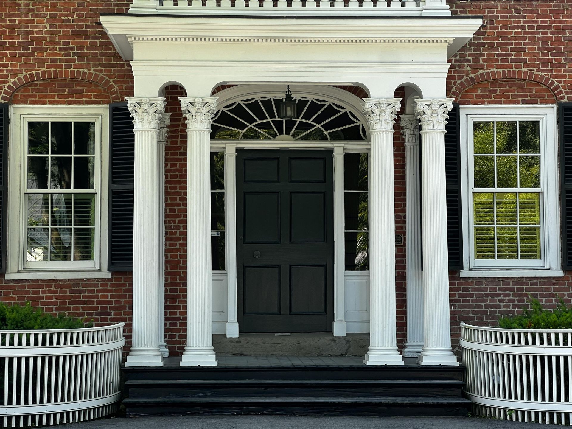 Front entrance of a brick building with white columns, black door, and windows on either side