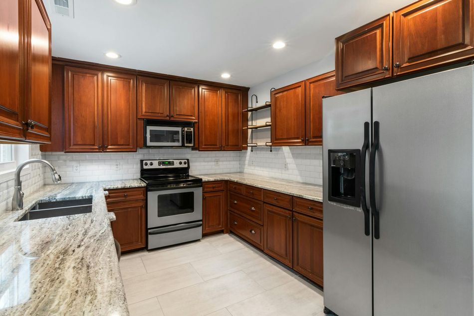 Modern kitchen with cherry cabinets, stainless steel appliances, white tile backsplash, and granite countertops
