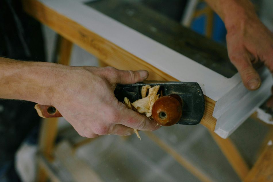 Hands planing a white wooden board with a handheld planer in a workshop