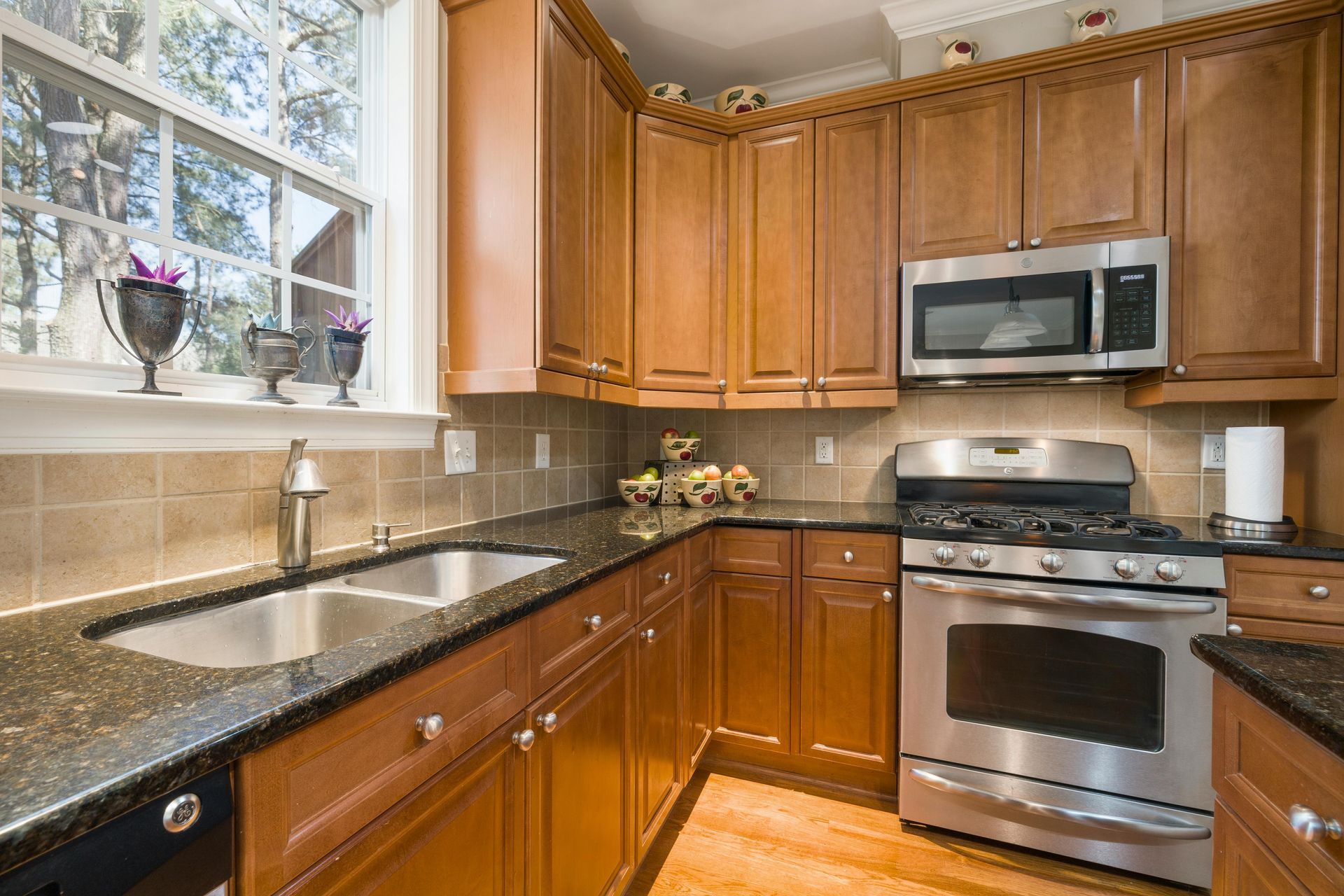 Modern kitchen with wood cabinets, black granite counters, stainless steel appliances, and a window over the sink