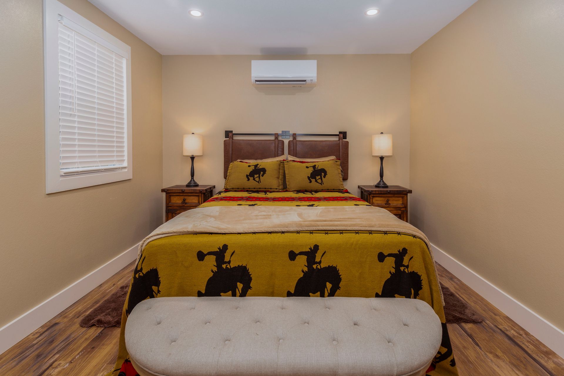 A bedroom with a bed , two nightstands , a bench and a window.