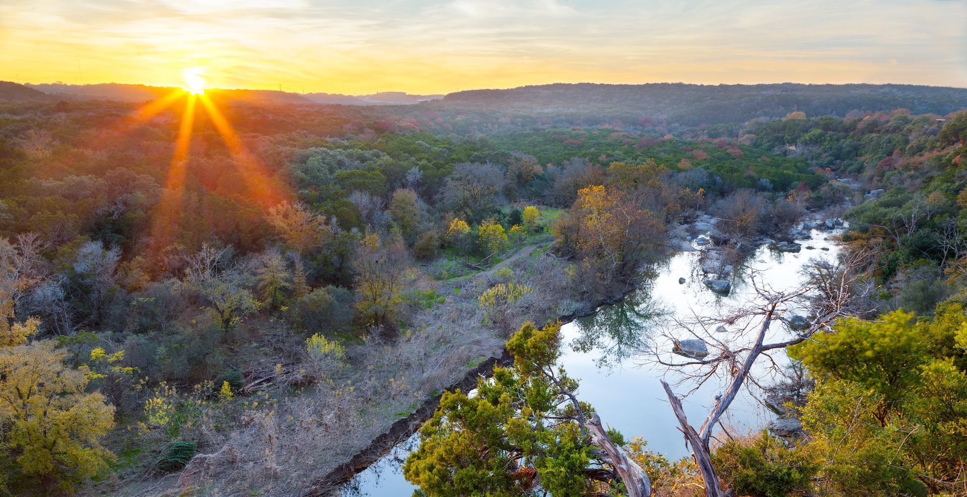 The sun is setting over a river surrounded by trees.