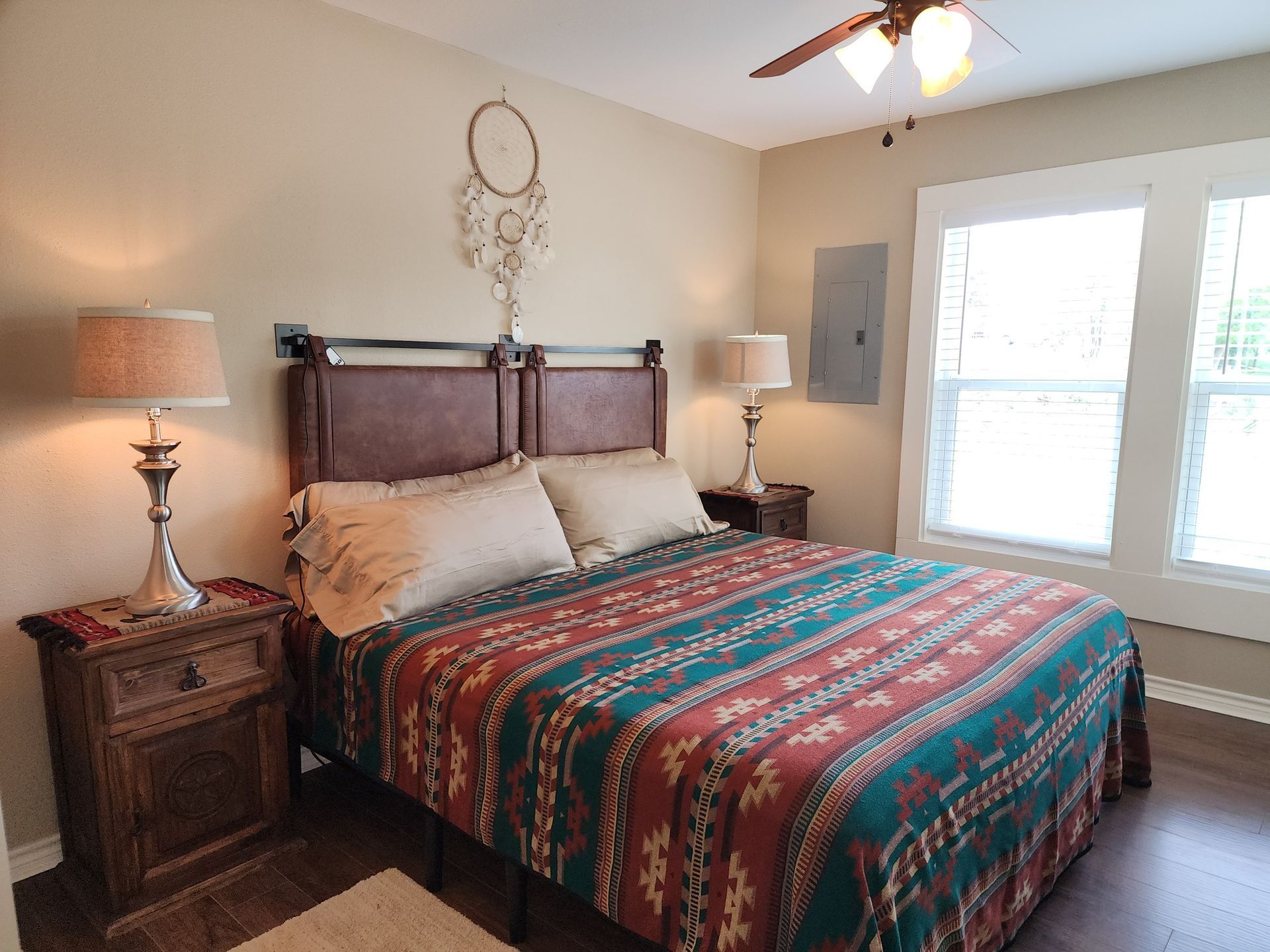A bedroom with a bed , two nightstands , two lamps and a ceiling fan.