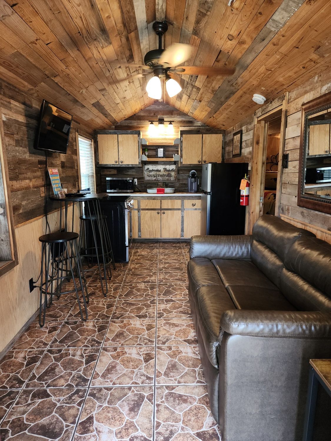 A living room with a couch and a kitchen with a ceiling fan.
