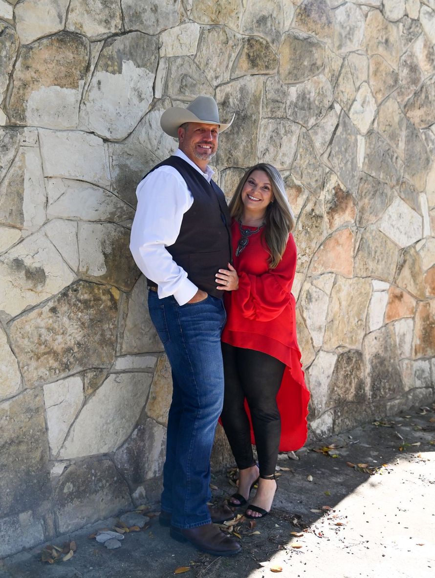 A man and a woman are standing next to each other in front of a stone wall.