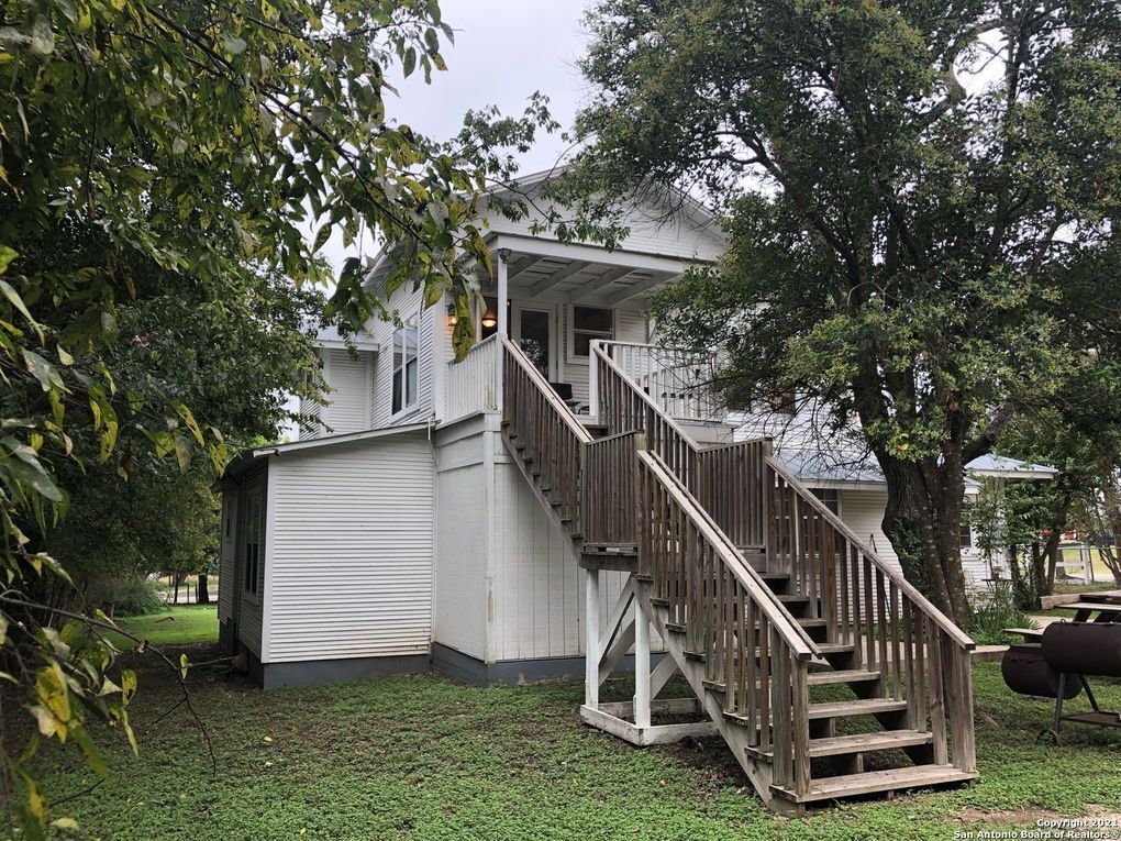 A white house with a wooden deck and stairs leading up to it.