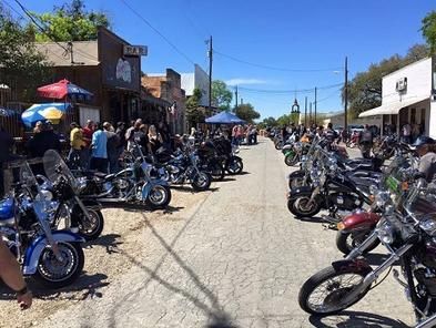 A row of motorcycles are parked on the side of the road in a small town.