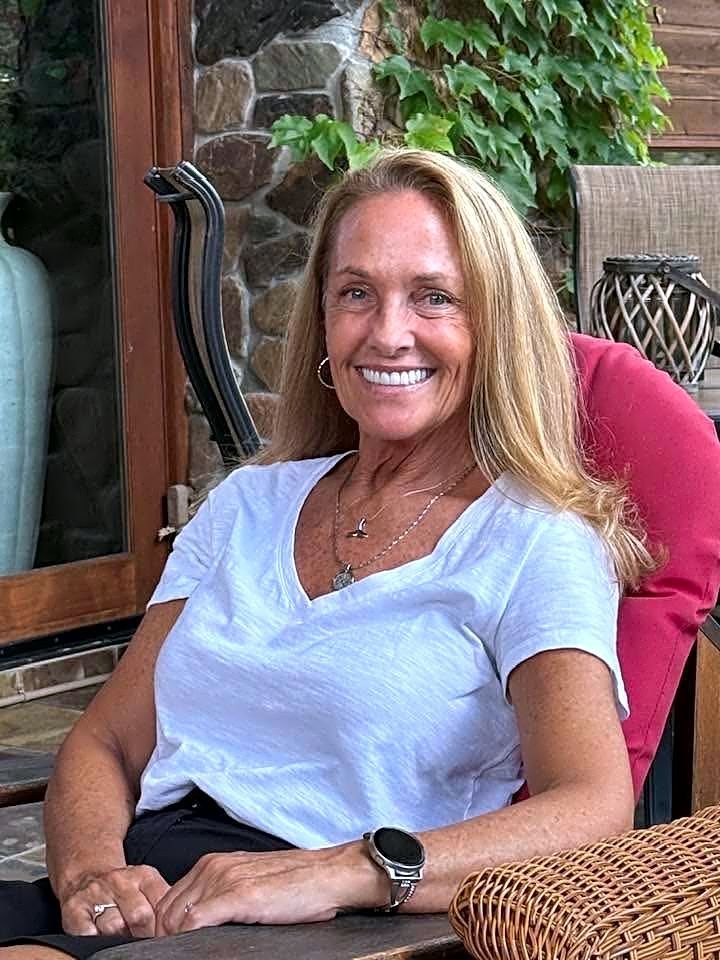 A woman is sitting at a desk with a laptop and a vase of flowers.