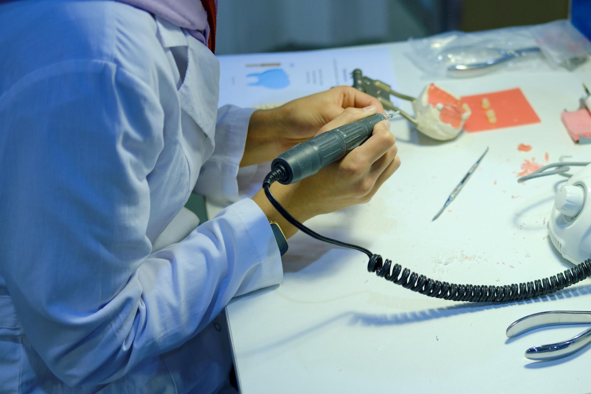 Person in lab coat using a rotary tool on a dental mold at a workbench with tools.