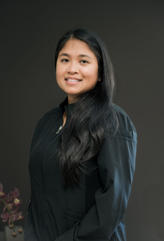 Woman with long dark hair smiles, wearing a black shirt. Dark background.