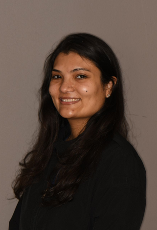 A smiling person with long dark hair, wearing a black top against a plain grey background.